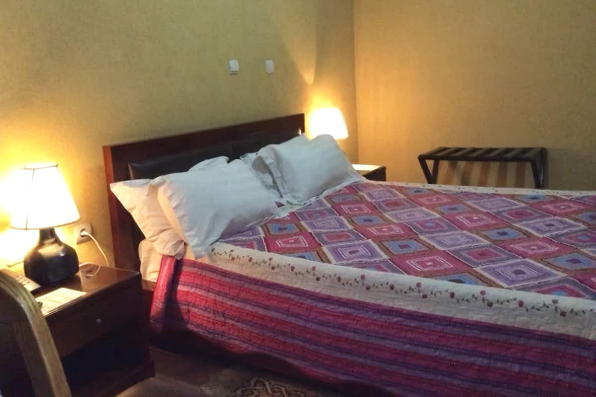 A neatly made bed with a patterned bedspread, two bedside lamps, and a wooden nightstand with a lamp.