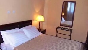 A hotel room with a bed, a nightstand with a lamp, a mirror, and a framed picture on the wall. - The Lions Den Hotel (Addis Ababa)