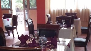 A dining area with tables set for two, chairs, and a view of the outdoors through large windows. - The Lions Den Hotel (Addis Ababa)