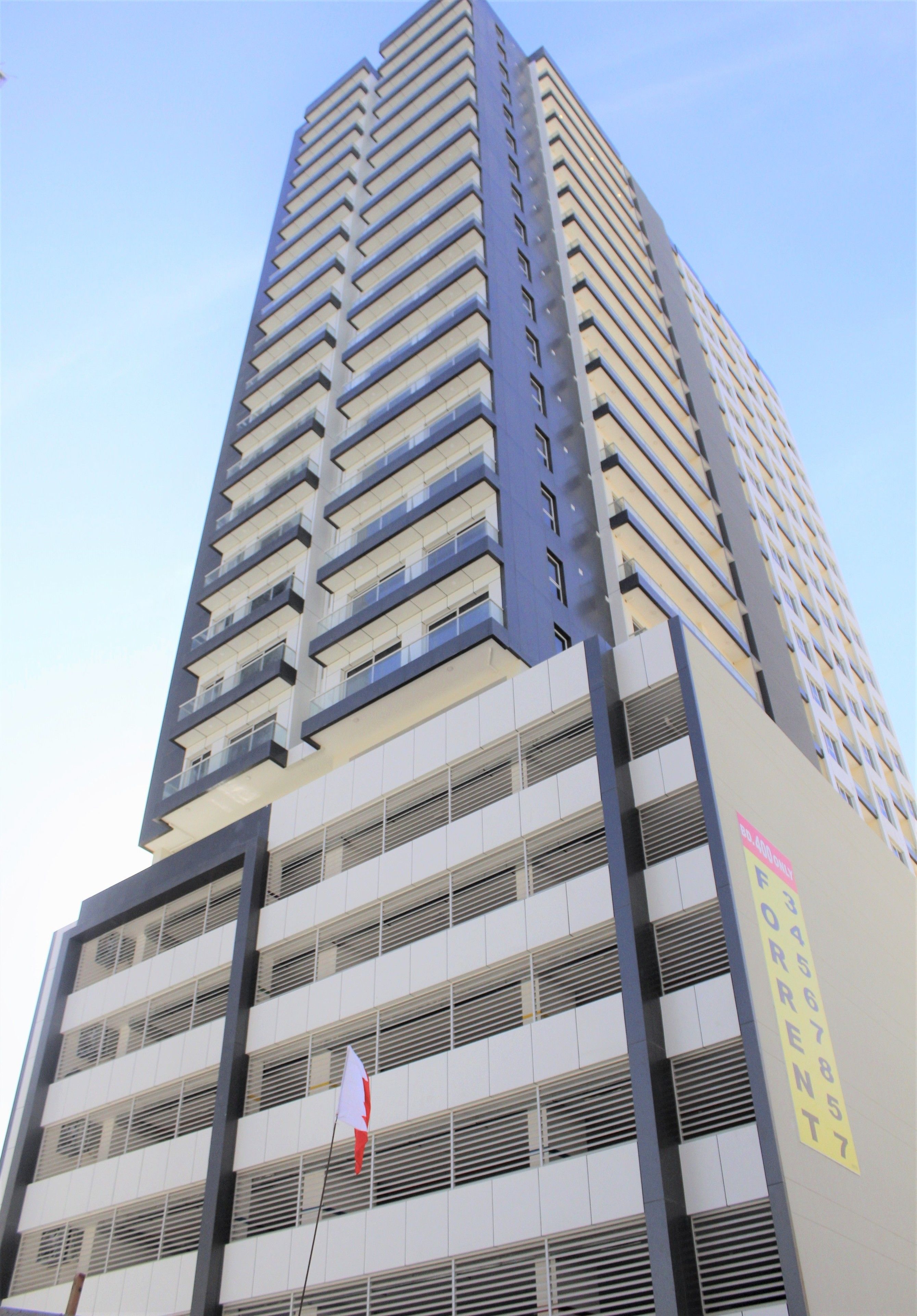 A high-rise building with multiple balconies and a sign indicating a rental property.