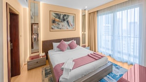 A modern hotel room with a large bed, a painting on the wall, a large window with curtains, and a wooden floor.
