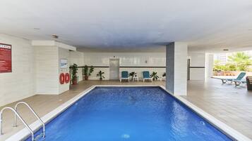Piscina interna com chão de azulejos, cadeira de salva-vidas e uma porta ao fundo.