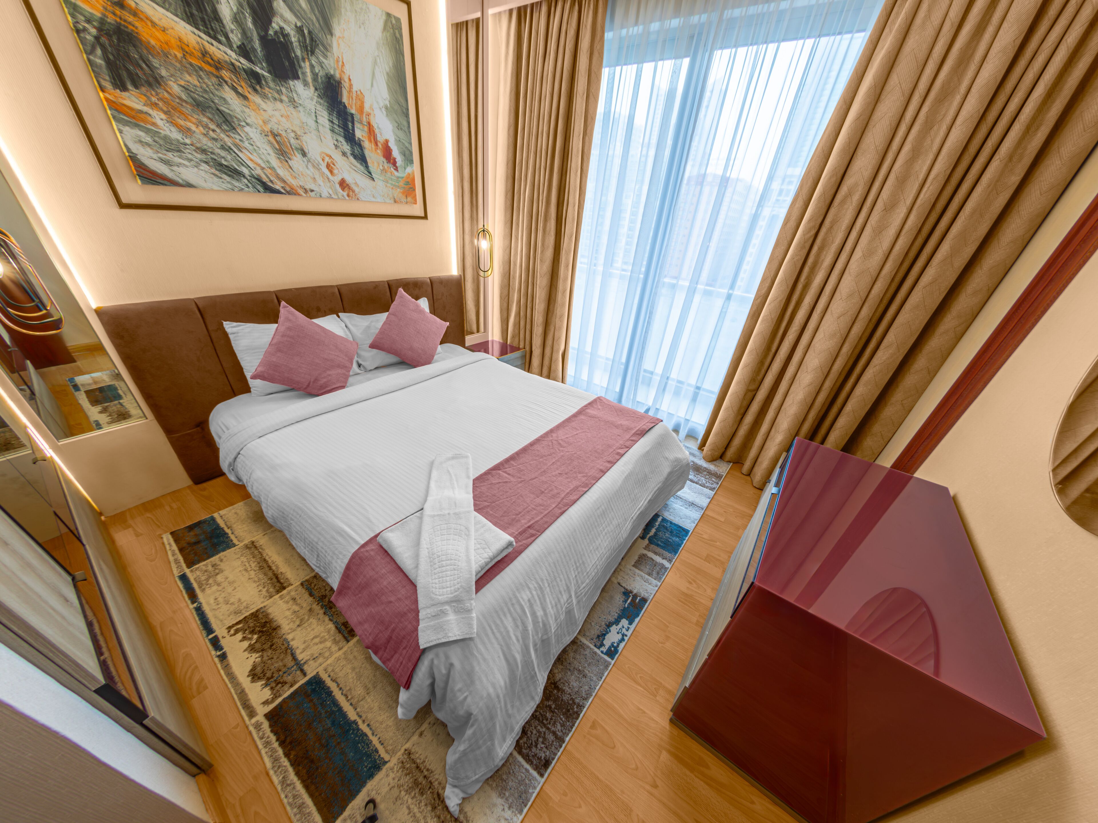 A hotel room with a large bed, a desk, a chair, a window with curtains, and a painting on the wall.