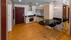 A modern kitchen with wooden cabinets, a black countertop, and a built-in oven. There is a dining area with a black table and bar stools.