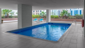 A swimming pool with blue tiles, white lounge chairs, and a view of buildings in the background.