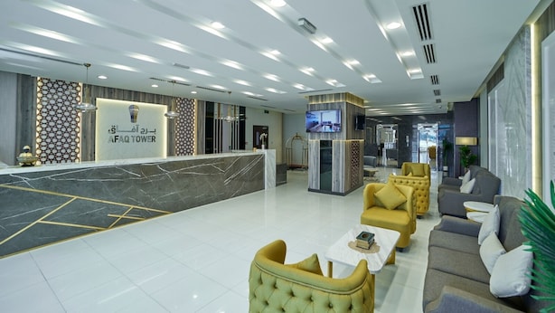 A modern hotel lobby with a reception desk, seating area, and a TV screen.