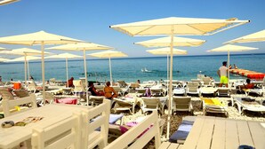 Une plage bordée de rangées de chaises longues et de parasols blancs, dont certaines sont occupées.