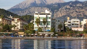 Un hôtel situé sur la côte, avec plusieurs étages, un espace piscine agrémenté de parasols et une vue sur les montagnes en arrière-plan.