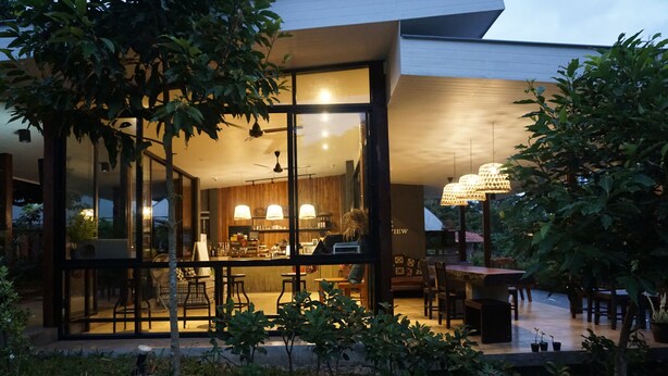 A modern house with large glass windows, a dining area with a table and chairs, and a kitchen visible through the windows. - Villa De View Chiang Dao (Chiang Dao)