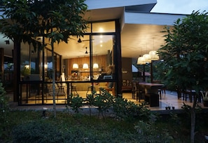 Una casa moderna con grandes ventanales, un comedor con mesa y sillas, y una cocina visible a través de los ventanales.