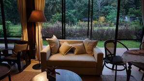 A cozy living area with a sofa, chairs, and a coffee table, featuring a large window with a view of lush greenery. - Villa De View Chiang Dao (Chiang Dao)