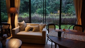 A room with a sofa, dining table, and chairs, large windows with a view of lush greenery. - Villa De View Chiang Dao (Chiang Dao)