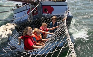 A group of people on a boat with a netted area, ropes, and a flag. - Zeilschip Liberté (Weesp)