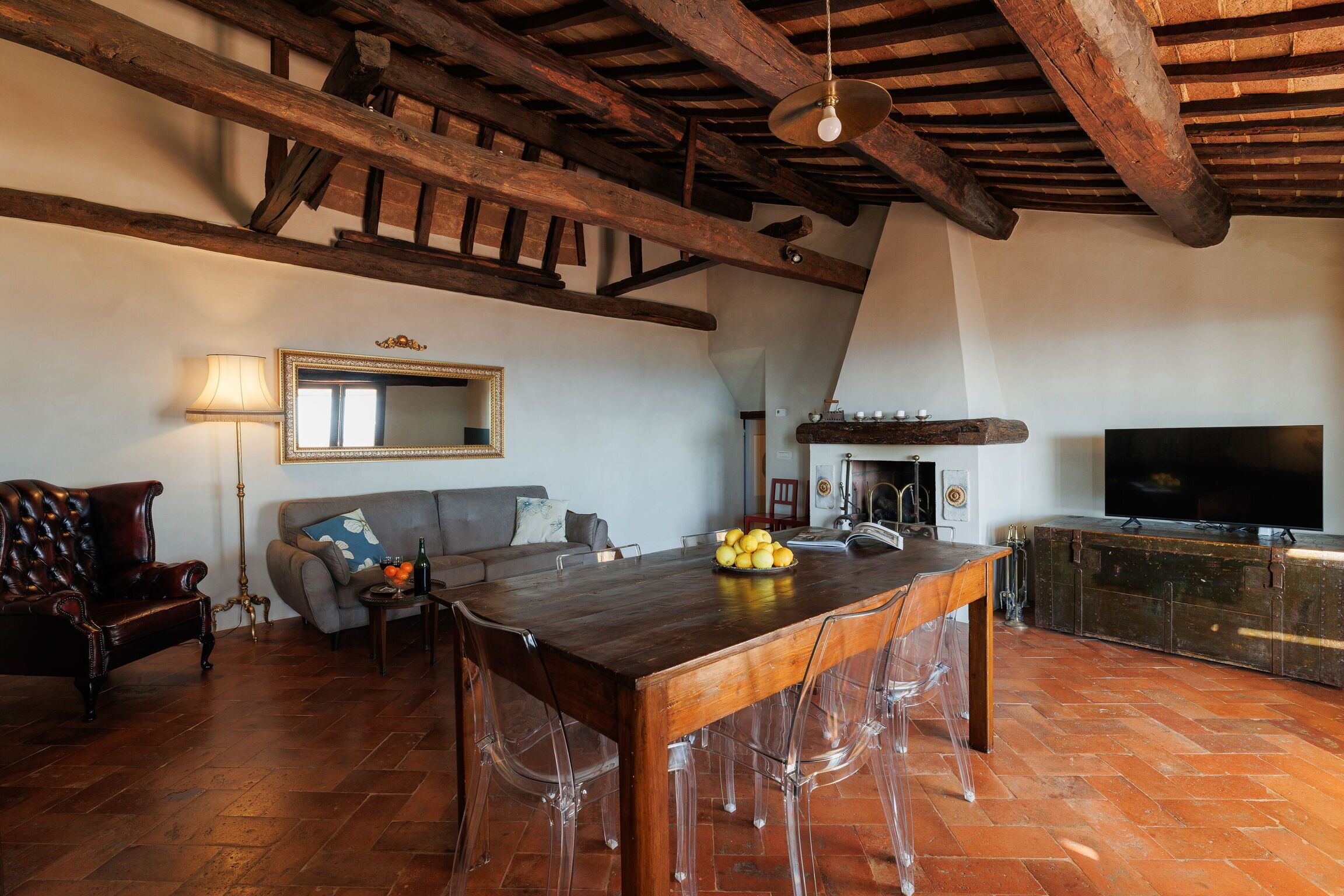 A spacious living area with a wooden dining table, clear chairs, a sofa, and a television.