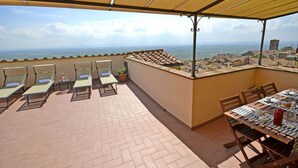 A terrace with sun loungers and a dining table, overlooking a coastal view. - La Terrazza Cortonese (Cortona)
