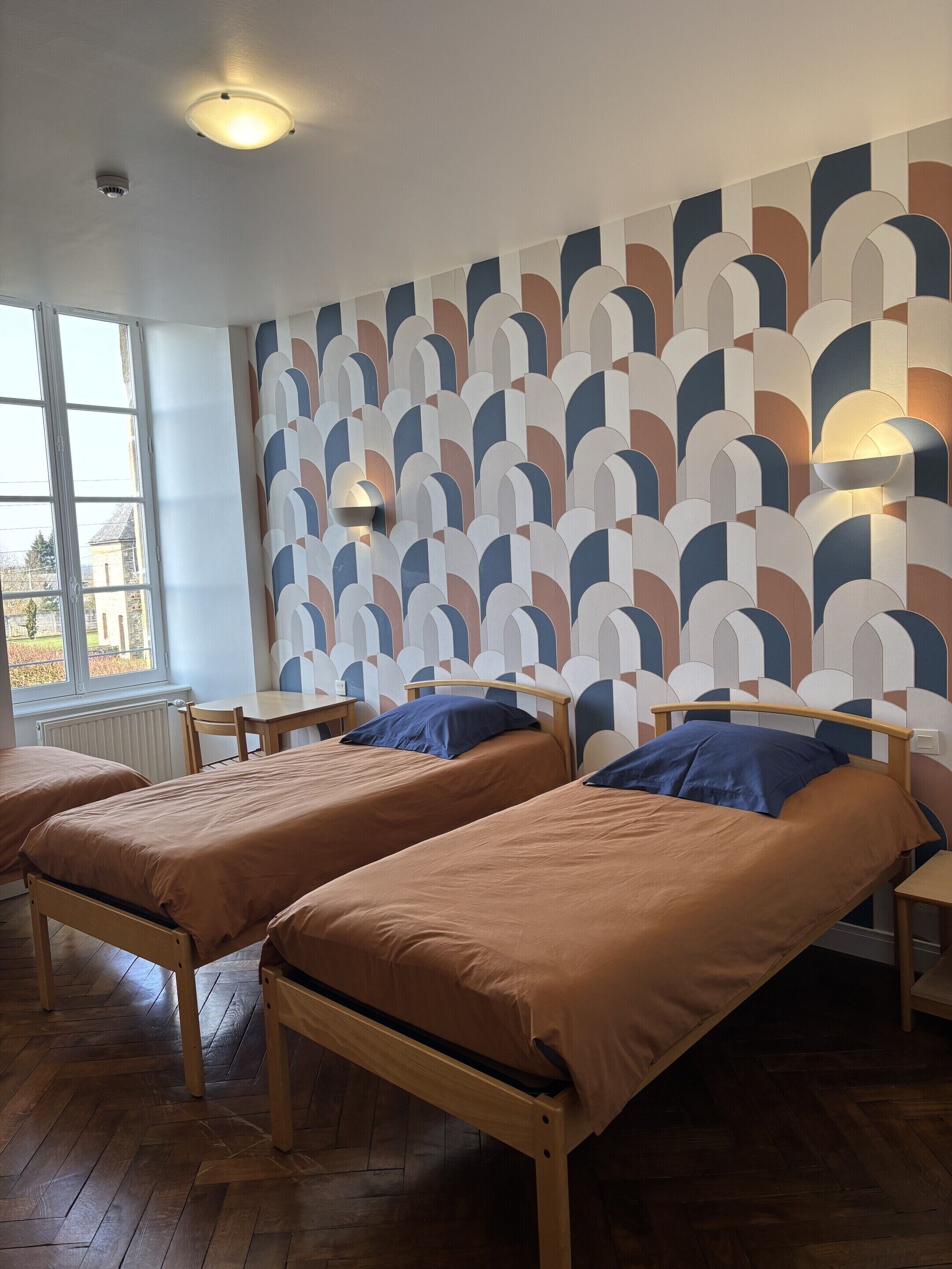 A room with two wooden beds, a window, and a patterned wall.