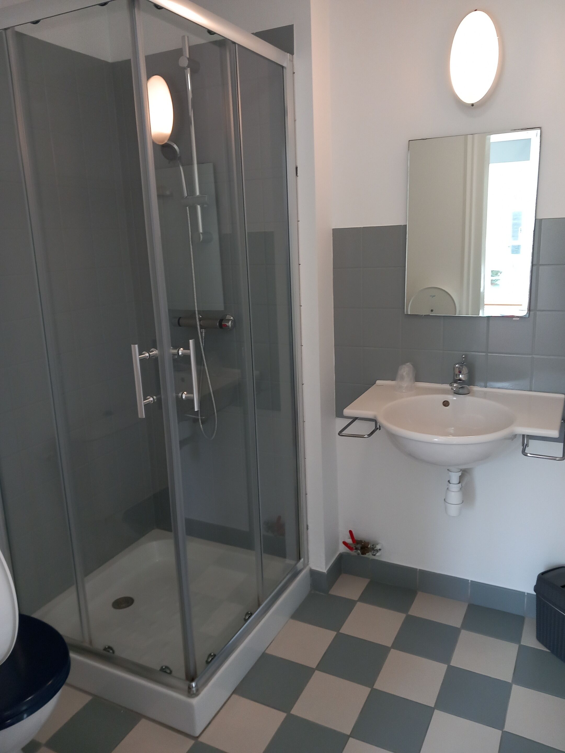 Un baño con ducha de mampara de vidrio, un lavamanos y un espejo.