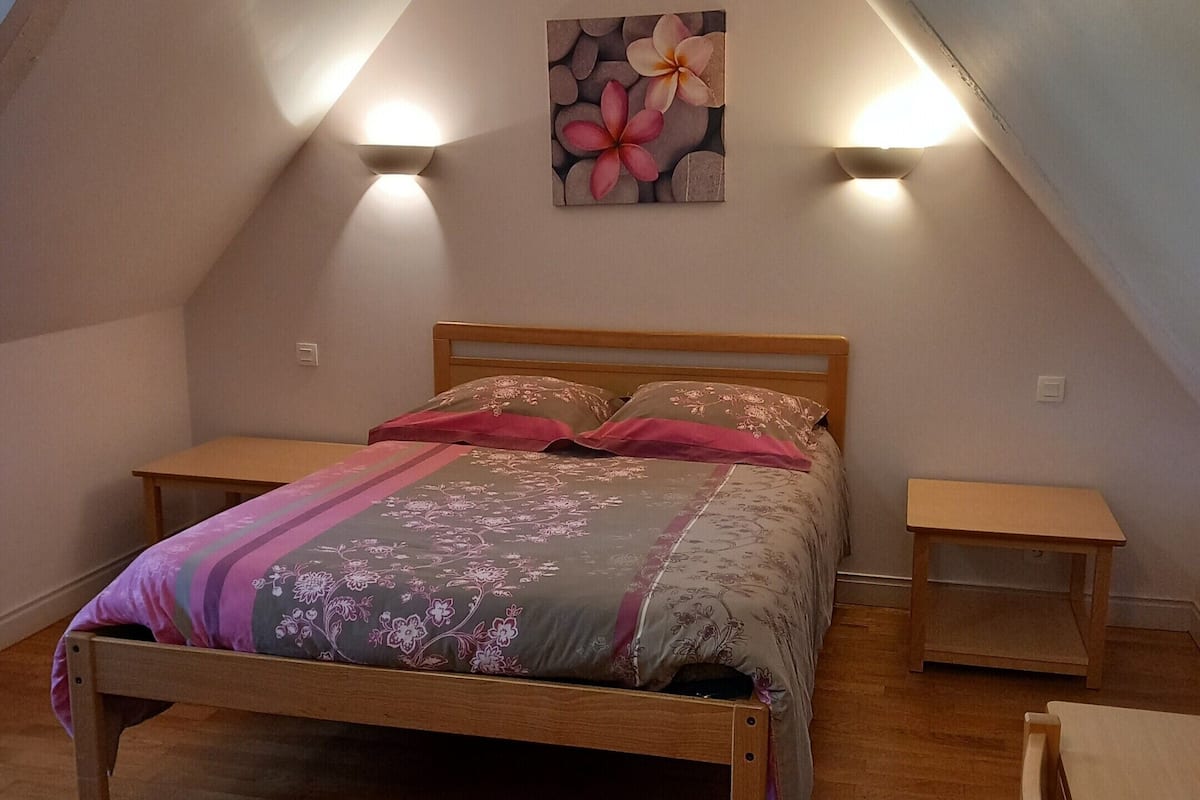 Een slaapkamer met een houten bed, een nachtkastje, een wandlamp en een schilderij van bloemen.