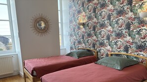 Une chambre avec deux lits simples, un luminaire fixé au mur et une fenêtre donnant sur un paysage agréable.