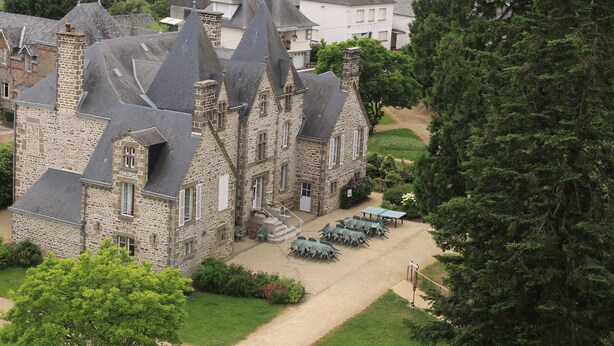 Un bâtiment en pierre doté de nombreuses cheminées et d’une cour pavée avec des espaces de repos en plein air.