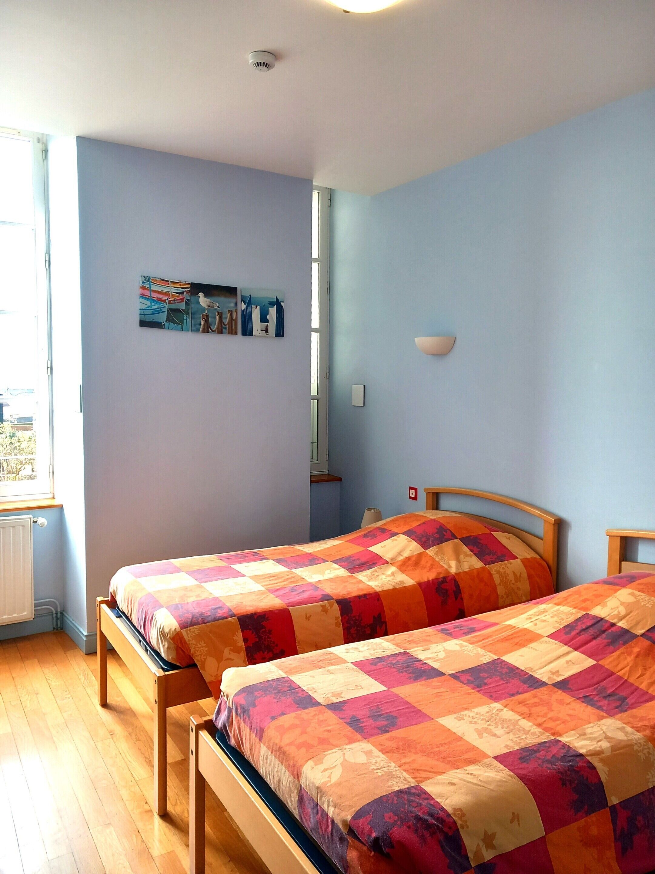 A bedroom with two wooden beds, a window, and a wall-mounted light fixture.