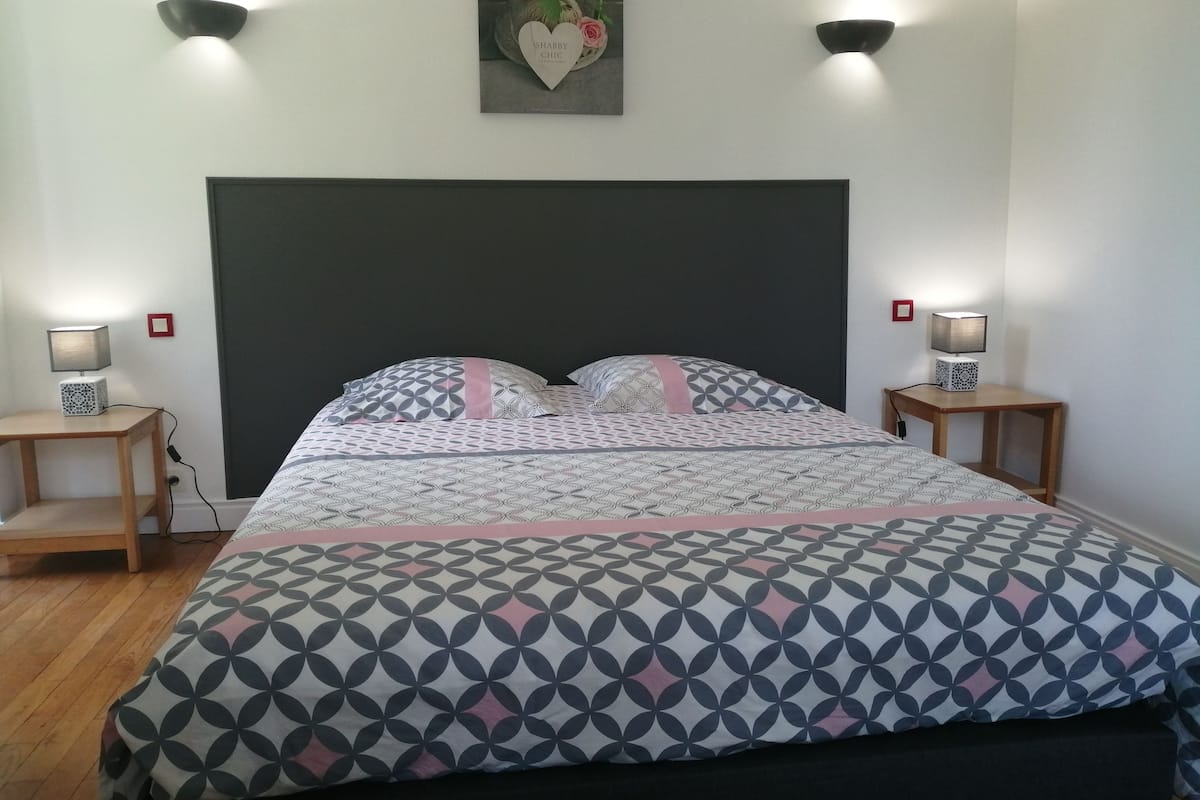 Een net opgemaakt bed met beddengoed met patroon, twee nachtkastjes met lampen, en een wandlamp.