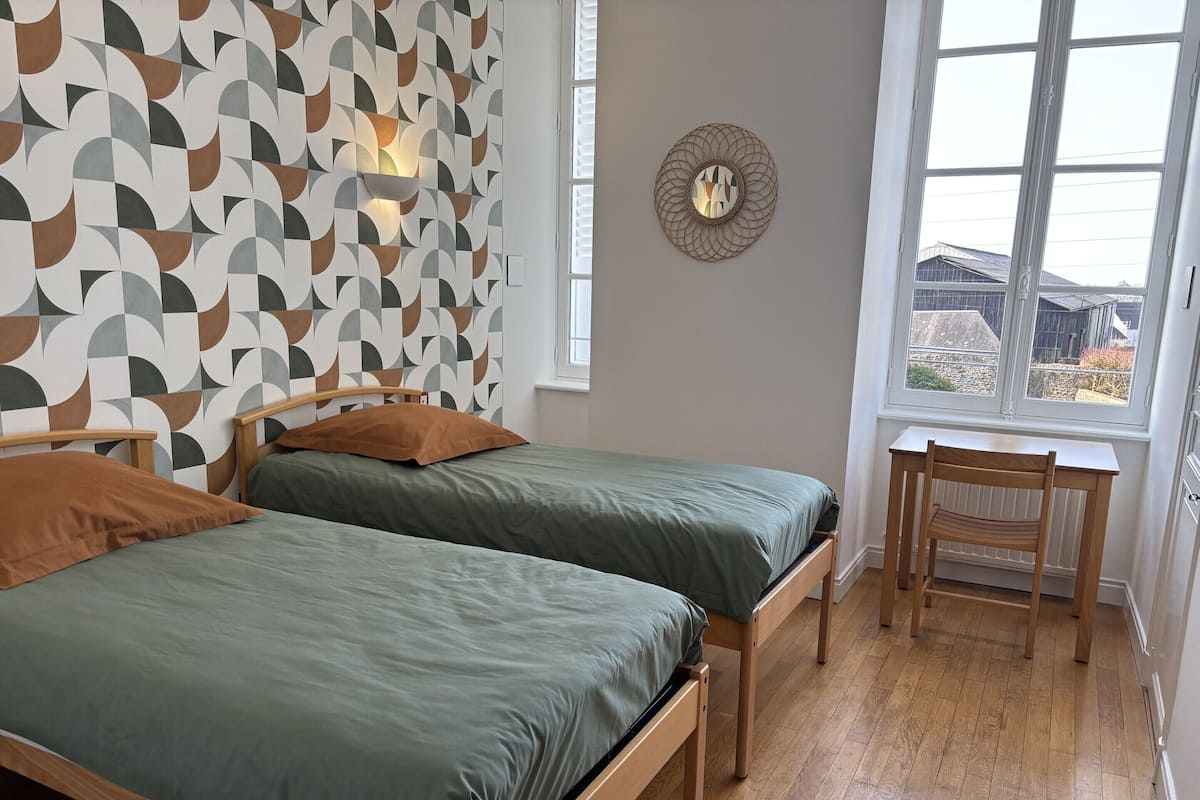 Een slaapkamer met twee bedden, een houten stoel, een raam met uitzicht en een muur met een geometrisch patroon.
