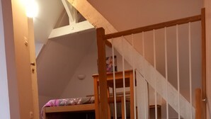 Un escalier en bois avec une rampe, menant à une chambre dotée d’un lit superposé et d’un lit recouvert d’une couvre-lit à motifs floraux.