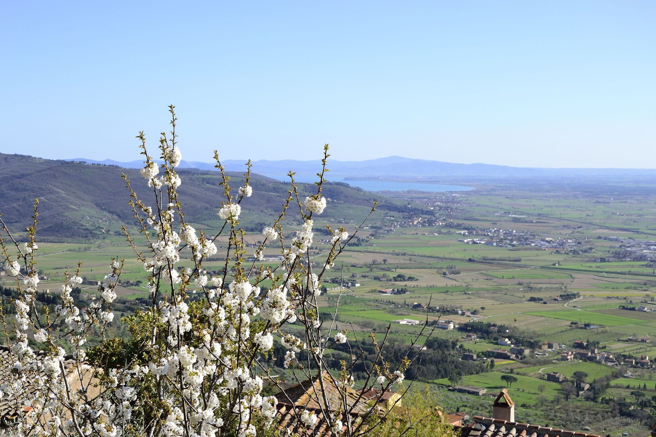 Paesaggio rurale con vista su una valle e un corpo d'acqua in lontananza.