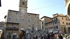 A historic building with a clock tower, multiple arches, and a bustling square with people. - Appartamento Il Teatro (Cortona)