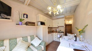 A cozy living room with a sofa, a dining table set for a meal, and a kitchen area with cabinets and a microwave. - Appartamento Il Teatro (Cortona)