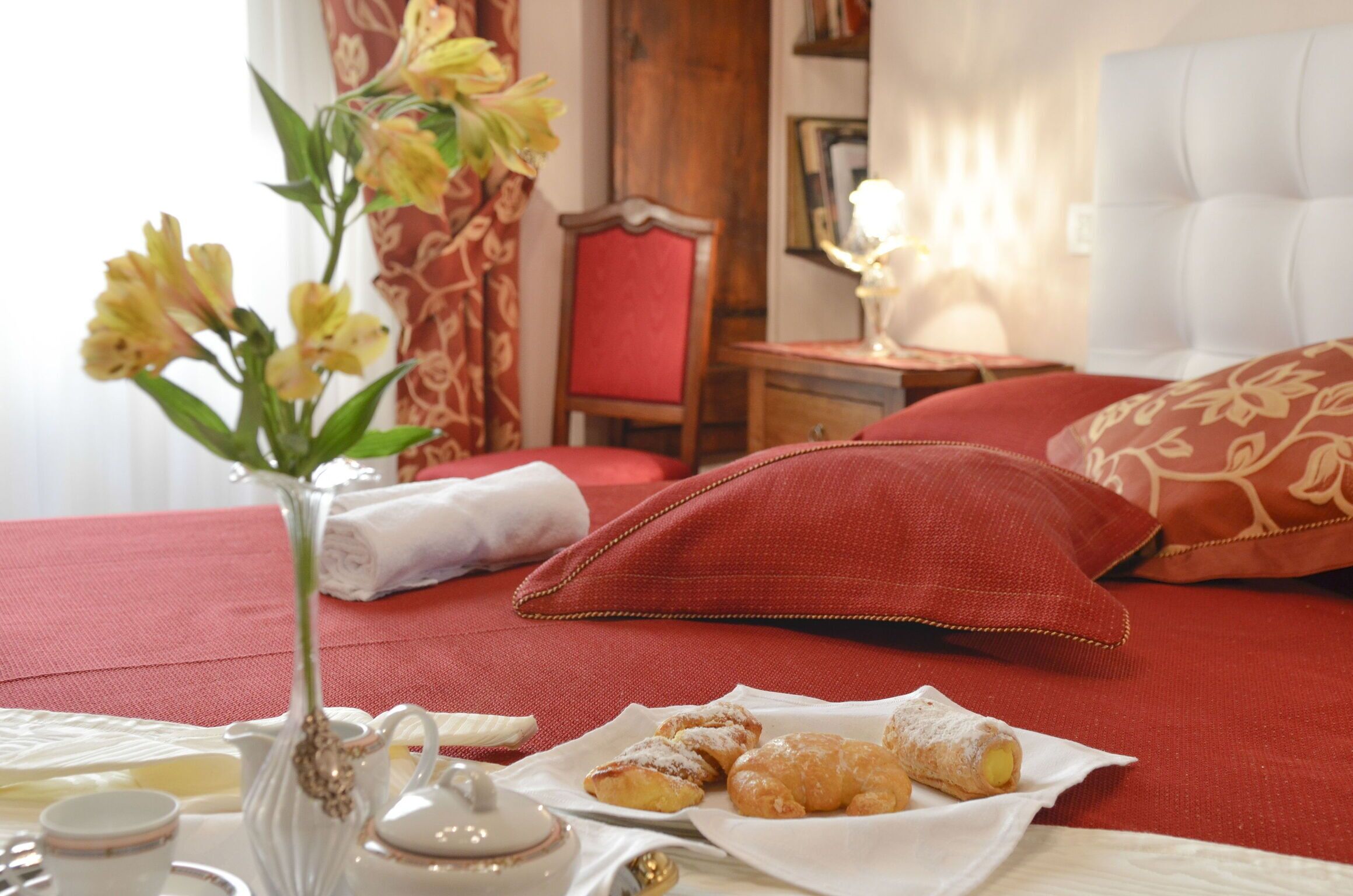 Un dormitorio ordenado con cama, almohadas, una mesita de noche con lámpara y una bandeja de pasteles.