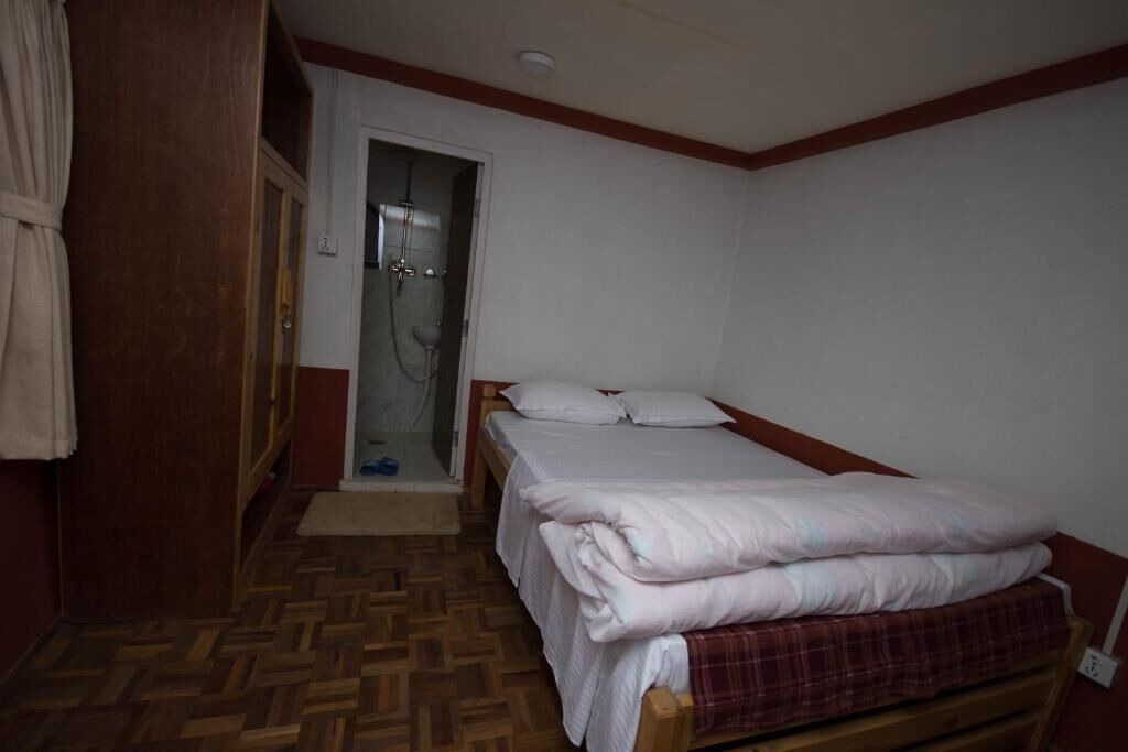 A small, single-bed room with a wooden floor, a shower, and a door leading to another room.