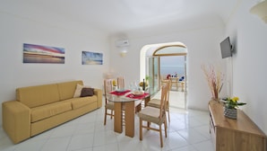 Una sala de estar moderna con un sofá, mesa de comedor, sillas y vista al mar a través de un arco.