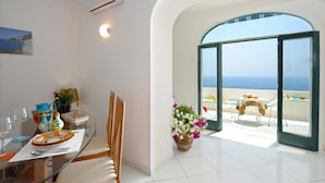 Una habitación moderna con una mesa de vidrio, sillas, una planta en maceta y vista al mar a través de una puerta abierta.