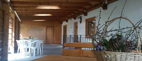 Interior de madera con una mesa, sillas, un banco y una cesta de mimbre con ramas.