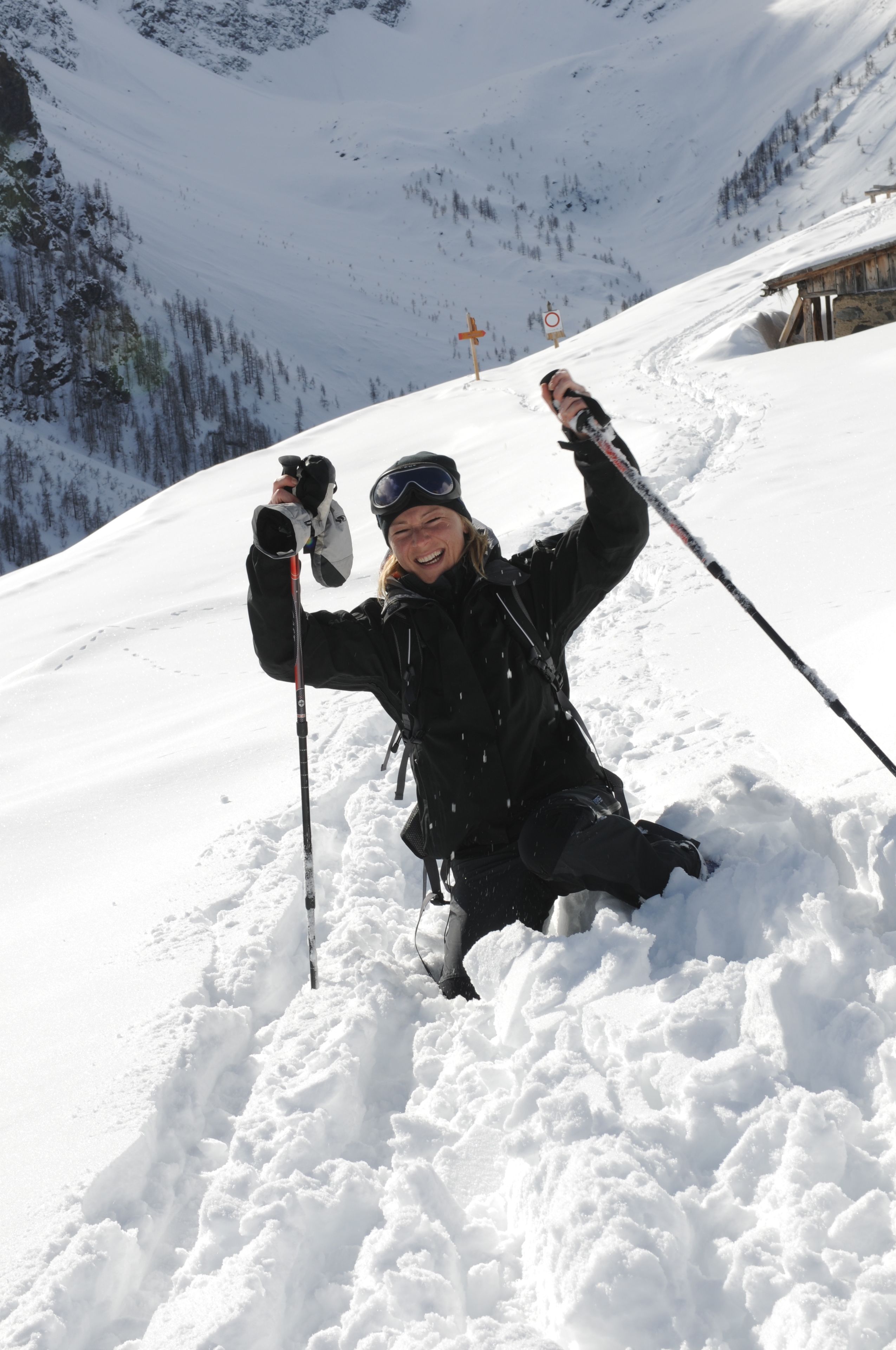 A person skiing on a snowy slope with ski poles, surrounded by snow and a mountainous backdrop.