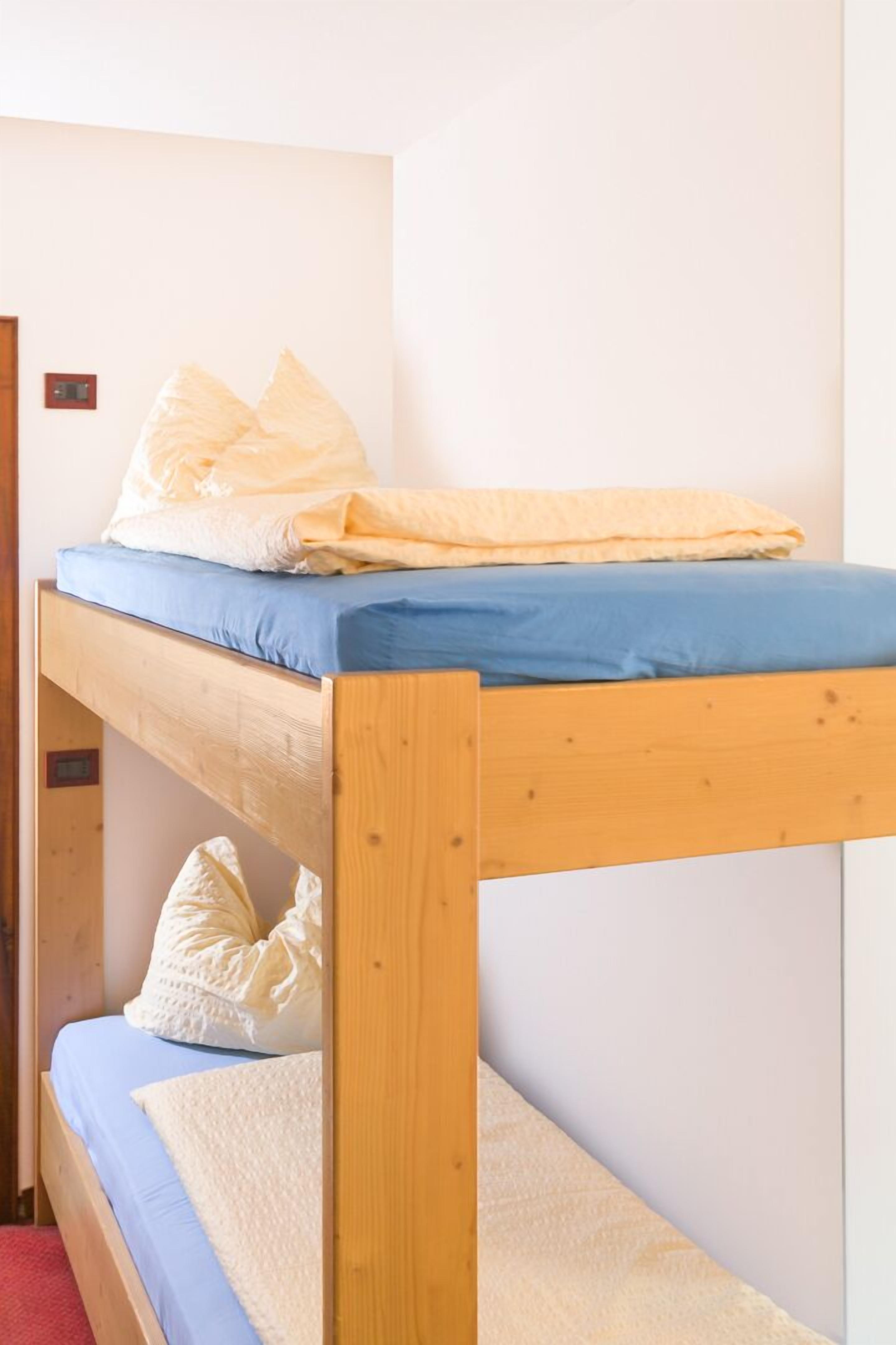A bunk bed with blue and white bedding, a wooden frame, and a plain white wall.
