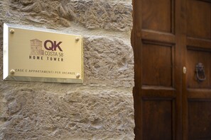 Une enseigne indiquant « QK Costa 58 Home Tower », avec un mur en pierre en arrière-plan et une porte en bois.