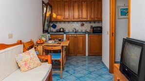 A compact living space with a kitchenette, a dining area, and a seating area with a sofa and TV. - Casa Emotion (Praiano)