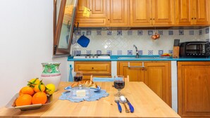 A kitchen with wooden cabinets, a blue countertop, a sink, a microwave, and a dining table with food and drinks. - Casa Emotion (Praiano)
