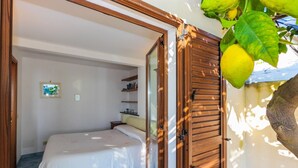 A bedroom with a bed, a wooden door, and a view of a garden. - Casa Emotion (Praiano)