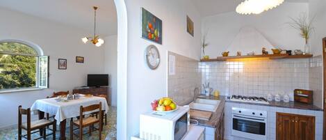 A compact kitchen with a dining area, a large window, and a tiled backsplash.
