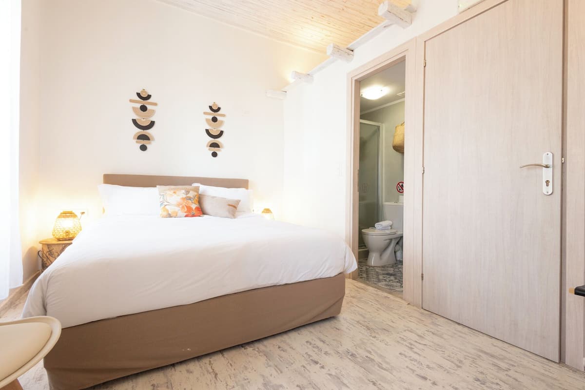 A bedroom with a bed, a nightstand, a wall-mounted light fixture, and a wooden wardrobe.