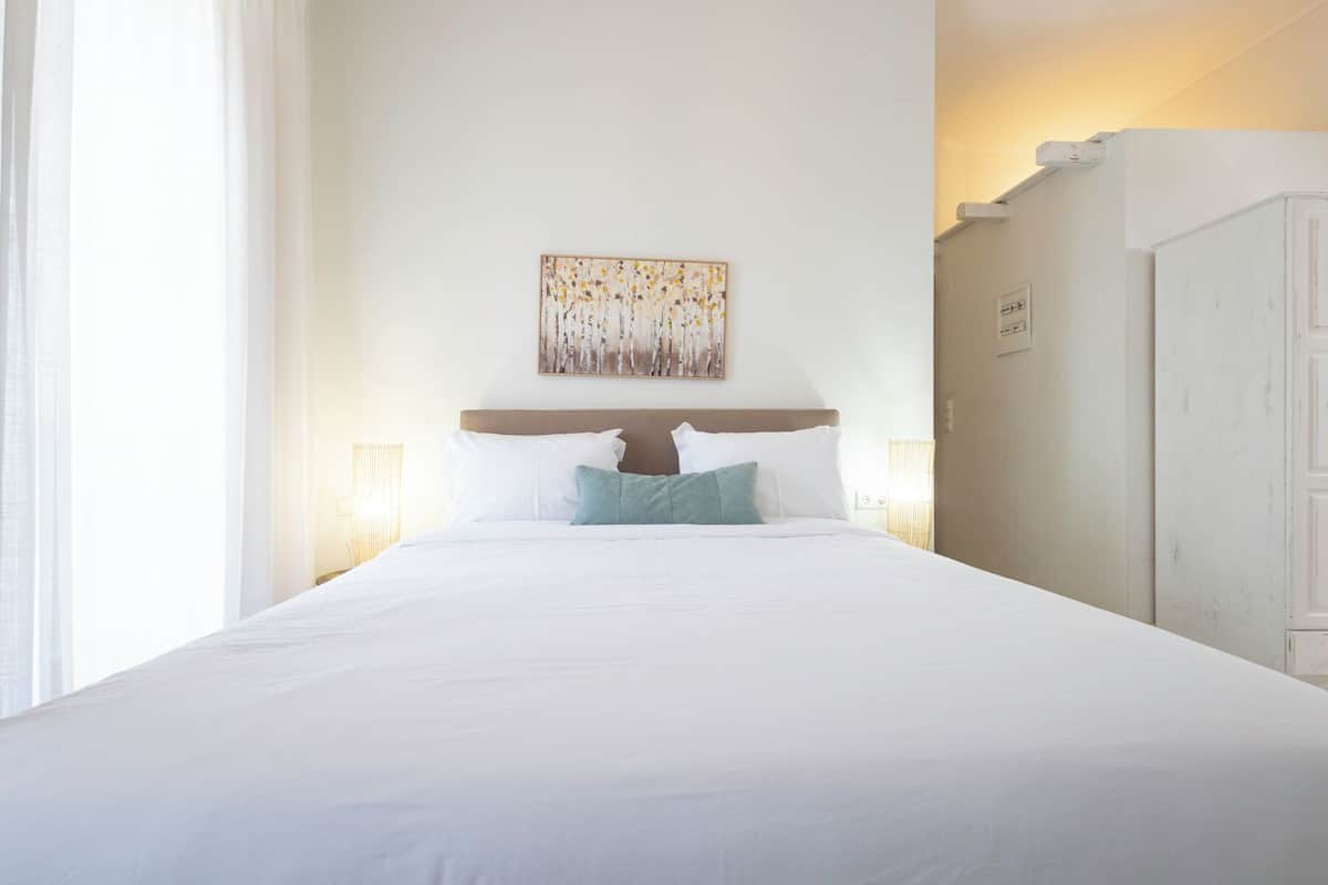 A hotel room with a large bed, a headboard, a painting on the wall, and a wardrobe.