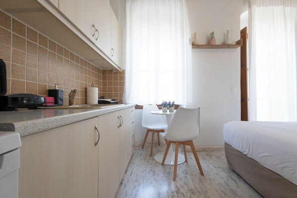 A compact kitchen with a dining area, a bed, and a window with curtains. - Sofia Areopoli (East Mani)