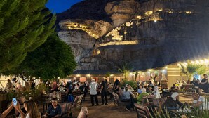 An outdoor seating area with tables and chairs, surrounded by a rocky cliff. - Hasan Zawaideh Camp (Wadi Rum)