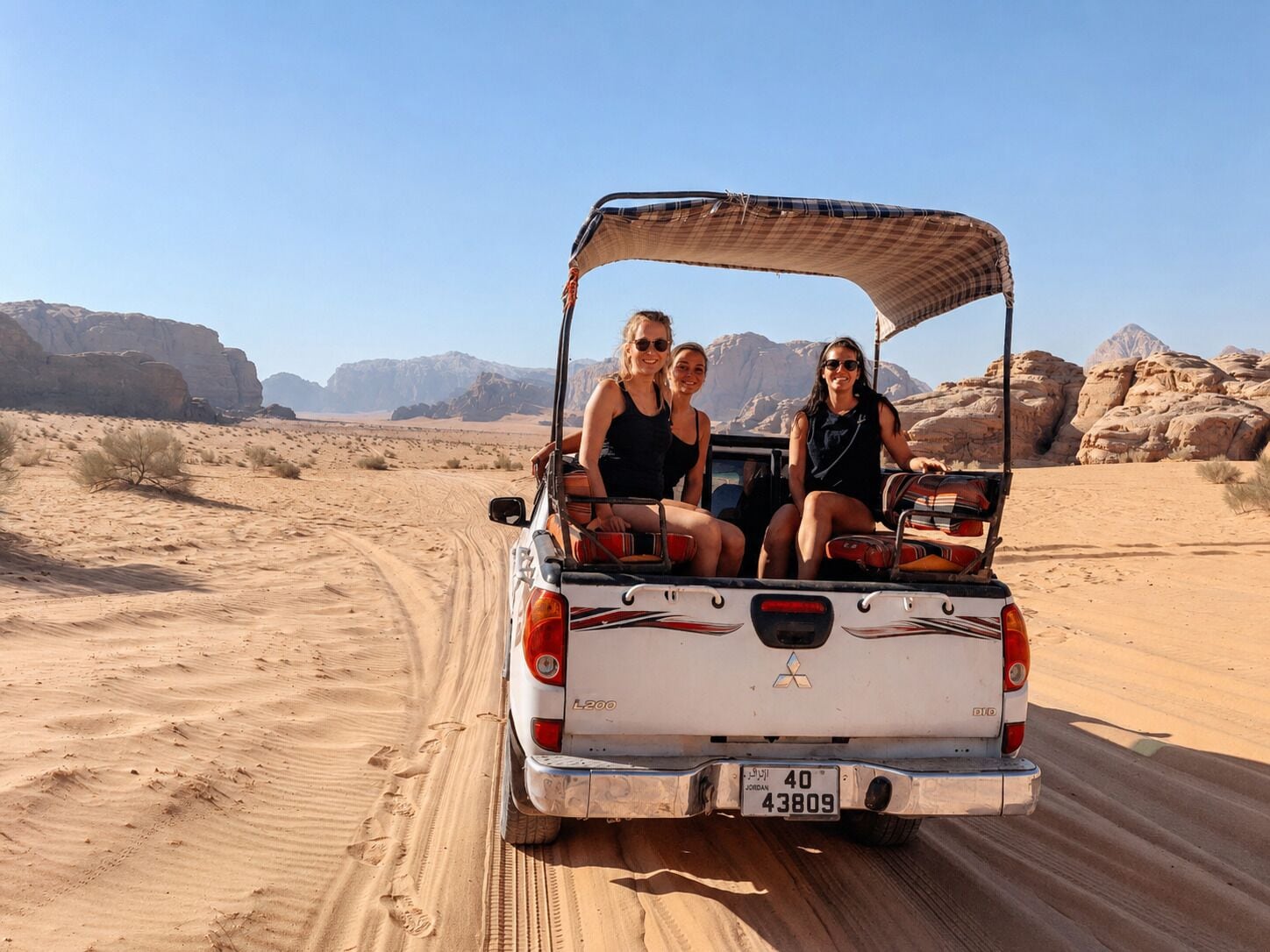 A desert landscape with a vehicle carrying three people.