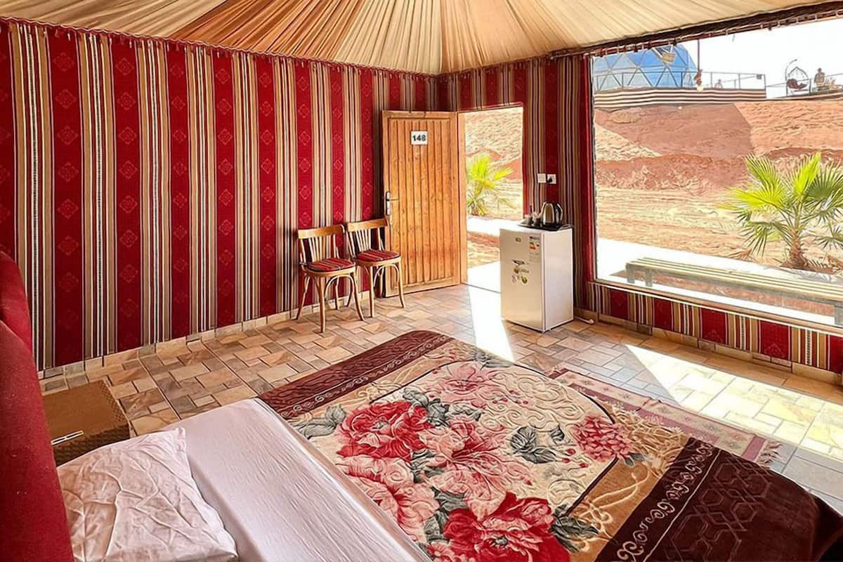 A room with a bed, two chairs, a small kitchenette, and a view of a desert landscape.