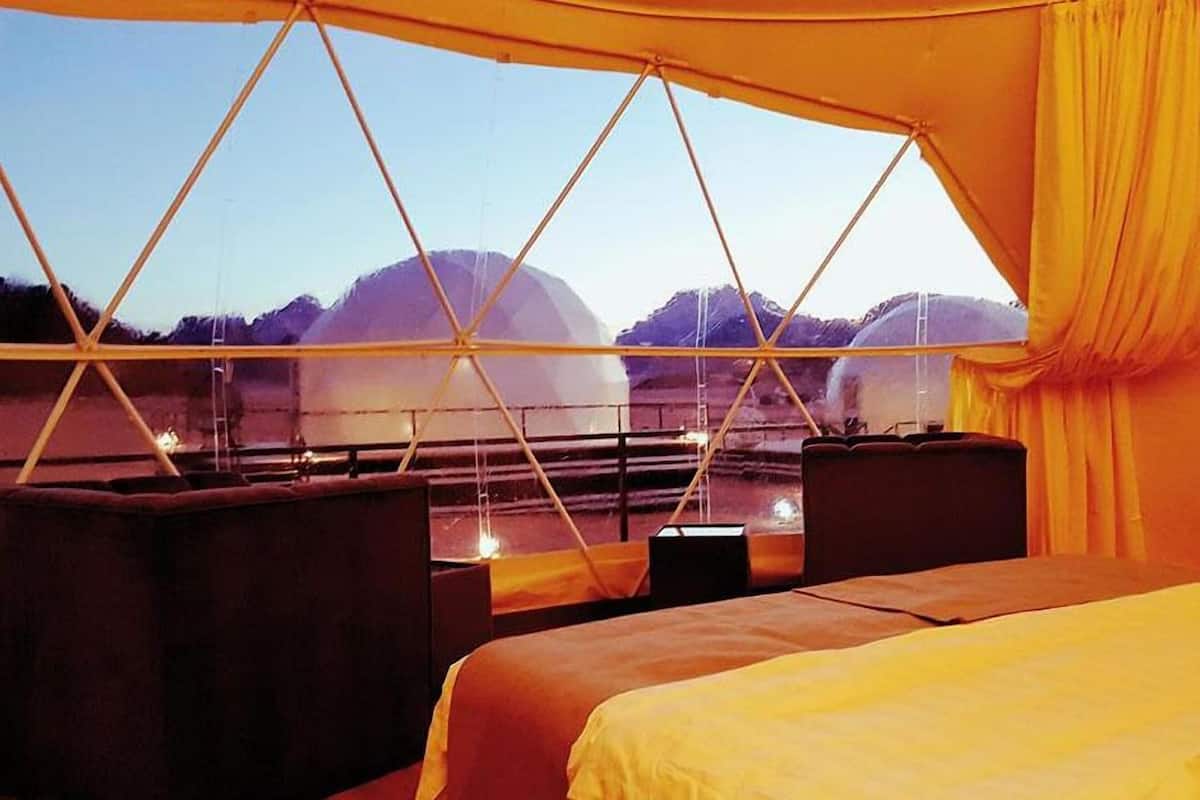 A tented room with a bed, two chairs, and a view of mountains.